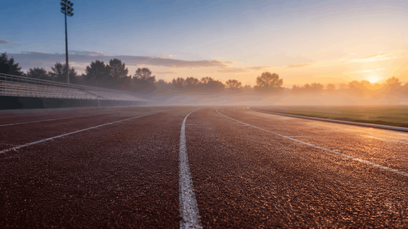 An empty outdoor running track at dawn with soft morning mist and golden light