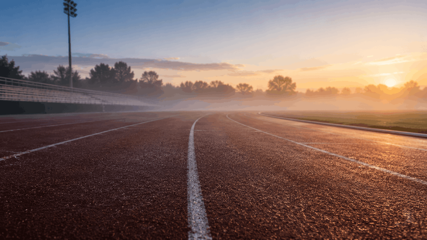 An empty outdoor running track at dawn with soft morning mist and golden light