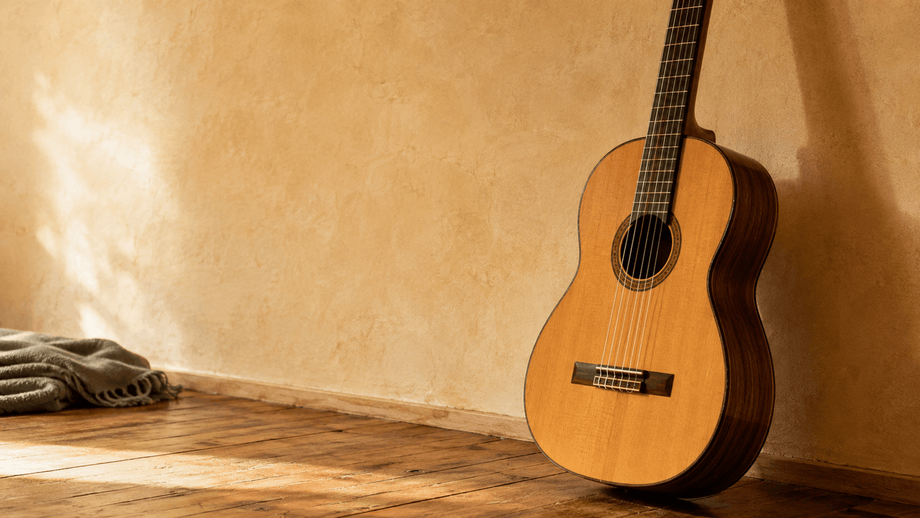 Acoustic guitar resting against a warm plaster wall on a bare wooden floor in morning light