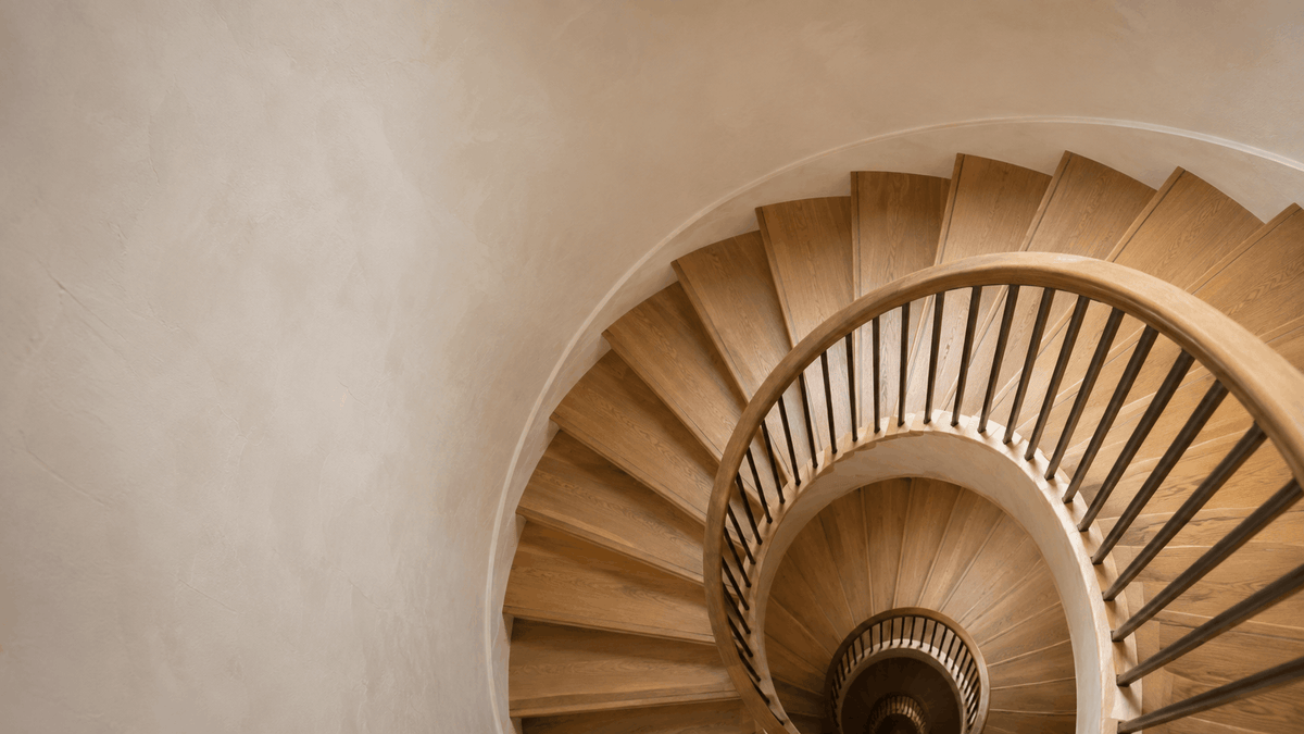 Wooden spiral staircase seen from above, curving down through daylight from a skylight