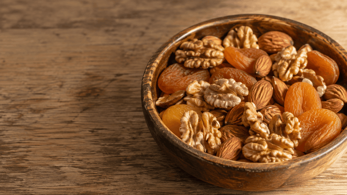Walnut halves, almonds, and dried apricots in a worn wooden bowl on a table