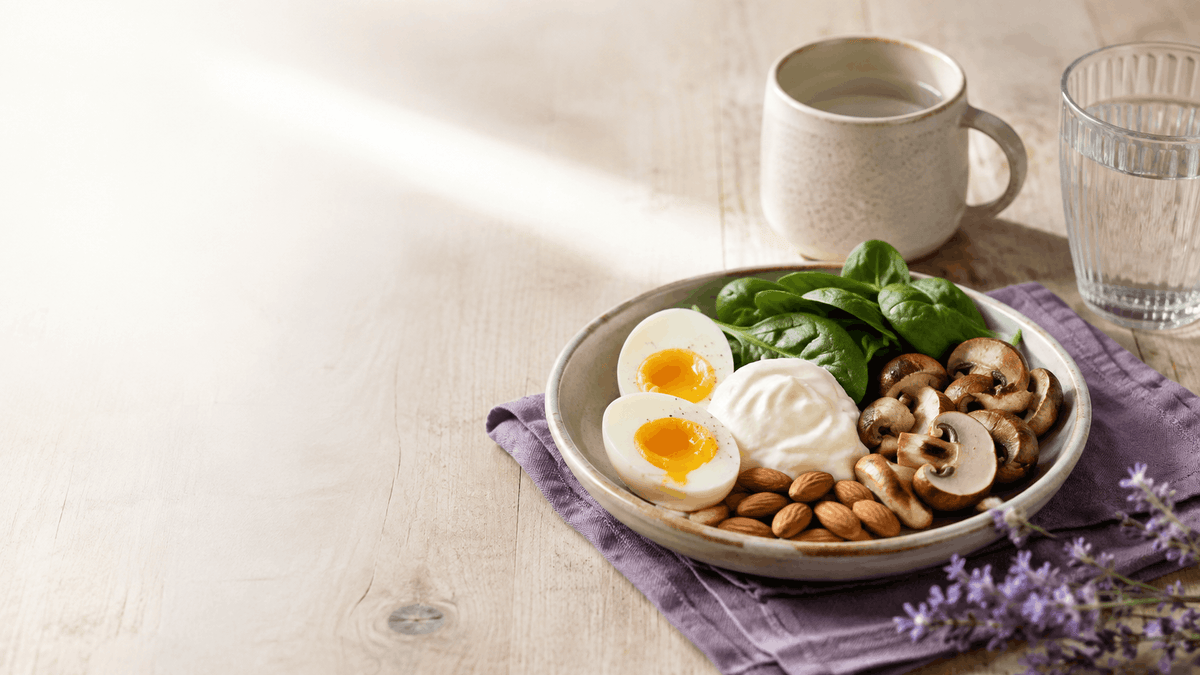 Breakfast bowl with soft-boiled eggs, spinach, mushrooms, yogurt, and almonds on purple linen in soft morning light
